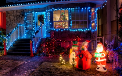 house with holiday lights and blow-up decorations with a christmas tree visible in the front window
