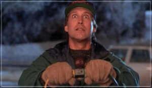 A man wearing gloves and a cap holds electrical plugs with a surprised expression, standing outdoors at night with a snowy background.