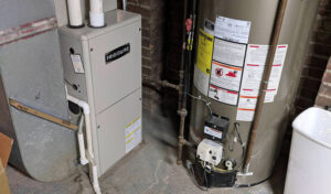 %Title% | Any Hour Services A furnace unit and a water heater are installed next to each other in a basement with exposed pipes and brick walls.