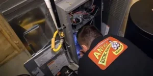 %Title% | Any Hour Services A technician in a black uniform is inspecting and working on the exposed interior of a home furnace unit.