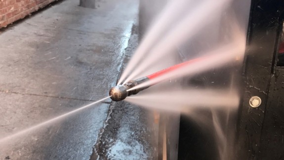 A high-pressure water jet nozzle sprays multiple streams of water onto a surface in an outdoor setting.