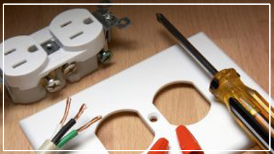 Close-up of electrical outlet components, a screwdriver, and exposed wires on a wooden surface, suggesting electrical work or repair.
