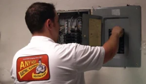 %Title% | Any Hour Services A technician in a branded shirt adjusts circuit breakers inside an open electrical panel mounted on a wall.