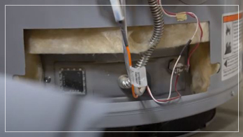 Close-up view of the lower section of a water heater, showing exposed insulation, electrical wiring, and metal components.