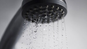 %Title% | Any Hour Services Close-up of water droplets falling from a showerhead, with a blurred gray background.
