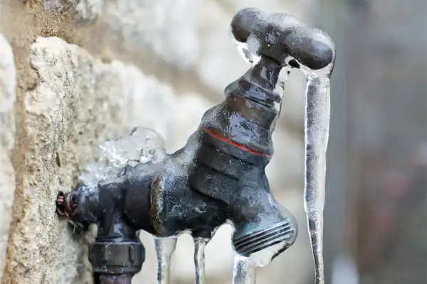 A metal outdoor faucet is frozen, with icicles hanging from it and a layer of ice covering the spout and handle.