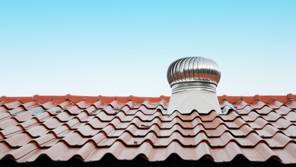 Red tiled roof with a metallic turbine vent set against a clear blue sky. The scene conveys a sense of calm and functionality in the architecture.