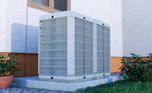 Two large outdoor HVAC units are installed on a concrete pad beside a house, with some plants and a potted plant nearby.