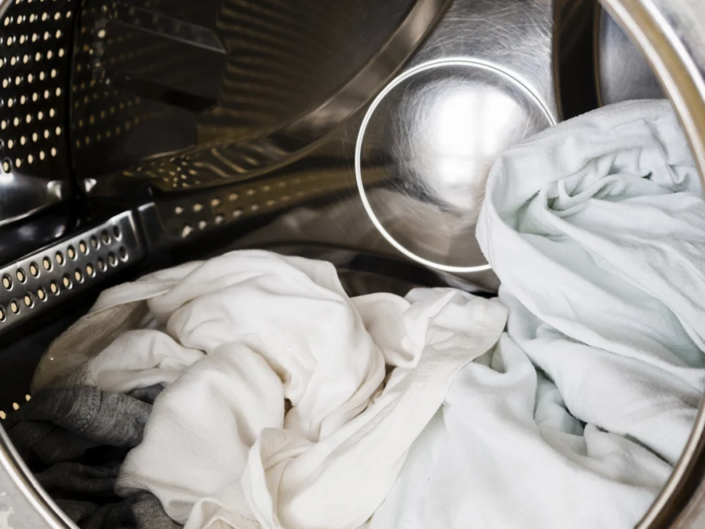 White clothes inside a stainless steel dryer drum, viewed from the open door.