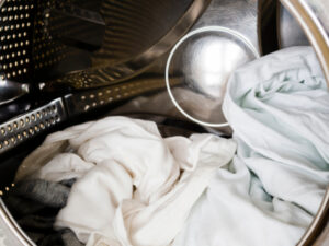 Dryer drum with several light-colored clothes inside, showing a close-up of laundry in the process of being dried.