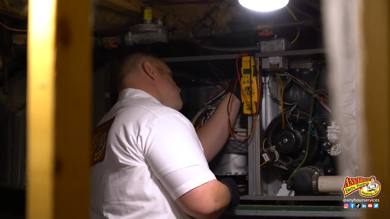 A technician in a white uniform inspects a furnace in a dimly lit space. He uses tools on the wiring, conveying focus and professionalism.