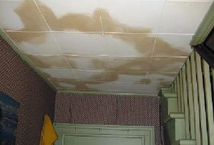 %Focuskw% | Any Hour Services Ceiling tiles with extensive brown water stains above a staircase and patterned wallpaper, indicating possible water damage.