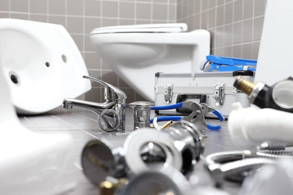Plumbing tools, fixtures, and parts are scattered on a bathroom floor near a toilet and gray tool case, suggesting ongoing plumbing work or repairs—perhaps supported by convenient plumbing financing options.