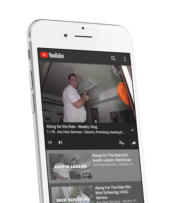 A smartphone displaying a YouTube video titled Along for the Ride - Weekly Vlog from Any Hour Services. The screen shows a person working indoors.