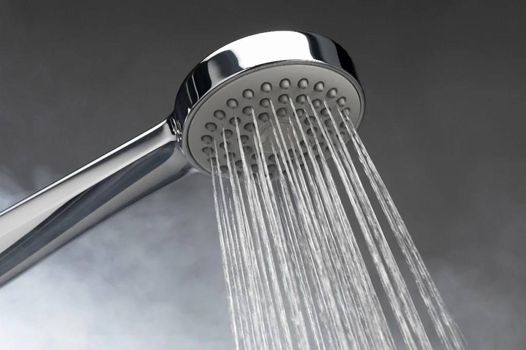 Close-up of a chrome handheld showerhead spraying water with steam or mist in the background.