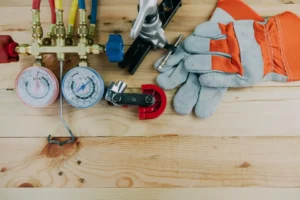 Assorted Heating and Cooling HVAC tools and a pair of work gloves are arranged on a wooden surface.