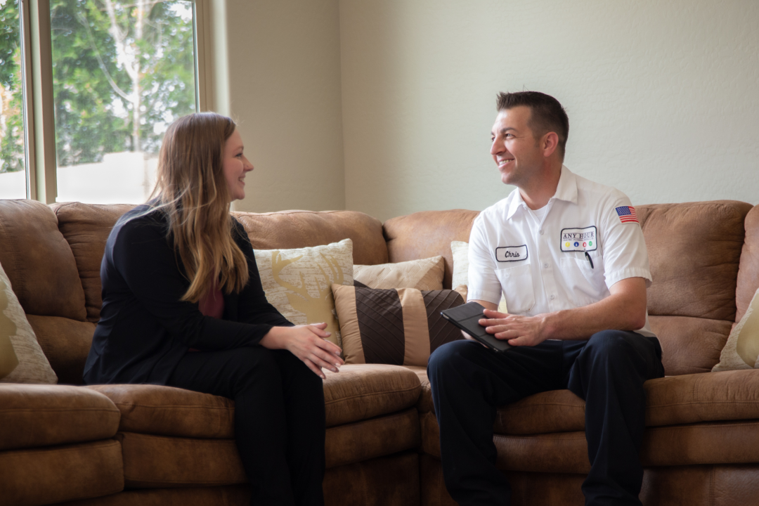 An Any Hour Technician and a home owner smile as they discuss something in the home owners living room