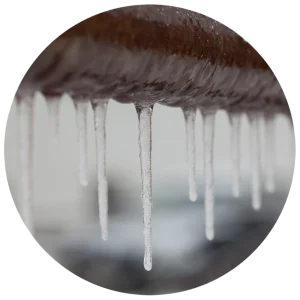 Close-up of icicles hanging from a rusted metal pipe against a blurred background. The image conveys a cold, wintery atmosphere and textural contrast.