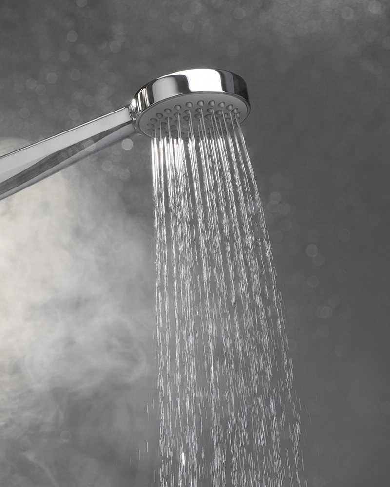 Shower head with water streaming against a gray background, surrounded by steam, creating a soothing and refreshing atmosphere.