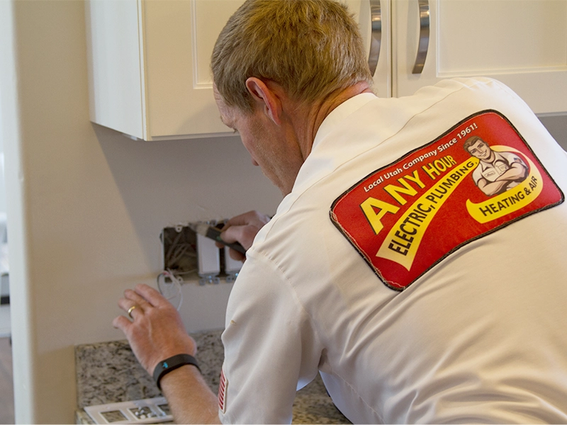 Electrician in uniform installs an electrical outlet on a kitchen wall. His shirt displays a company logo, conveying professionalism and focus.