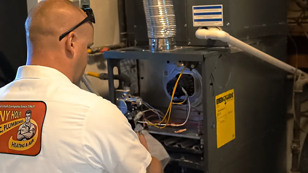 A person in a work uniform labeled Any Hour is inspecting a furnace system in a utility room. The scene conveys professionalism and focus.