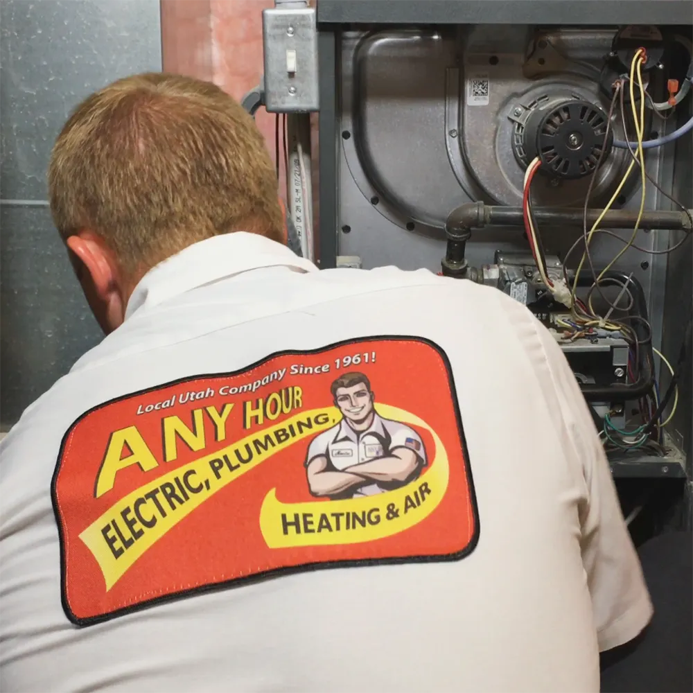 Technician in a white uniform with Any Hour Electric, Plumbing, Heating & Air logo works on a furnace, showcasing expertise and professionalism.