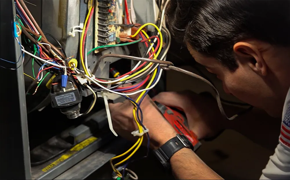 A technician repairs a furnace, focusing intently on tangled colorful wires and electronic components. The scene conveys concentration and technical skill.