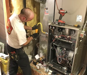 A person in a work uniform labeled Any Hour is inspecting a gas line system in a utility room. The scene conveys professionalism and focus.