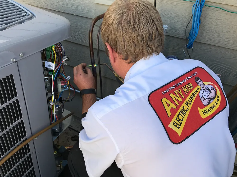 A technician in a branded shirt is working on an air conditioning unit outside a house. The scene conveys focus and expertise in HVAC repair.