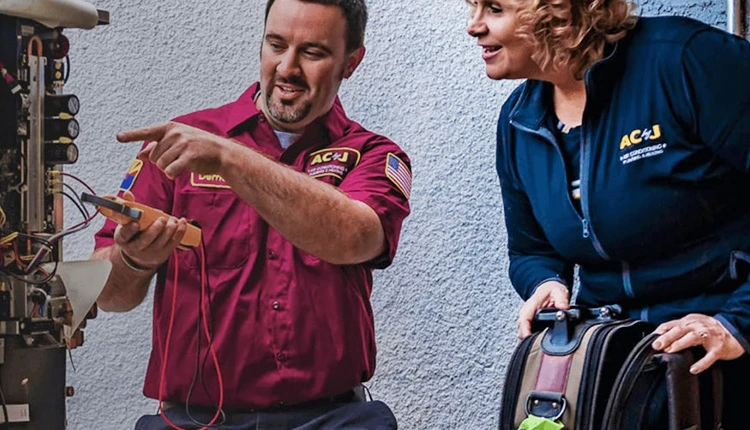 A technician in a red uniform explains a boiler system to a woman in a blue jacket. They appear engaged and focused. Tools and wires are visible.