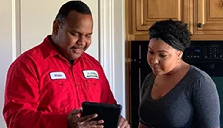 A technician in a red uniform shows a tablet to a woman in a kitchen. Both appear engaged and focused, creating a professional and informative tone.