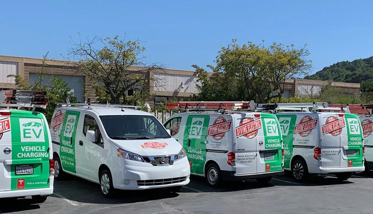 Four white vans with green EV Vehicle Charging graphics are parked in a lot. They're equipped with ladders, conveying a professional, eco-friendly tone.