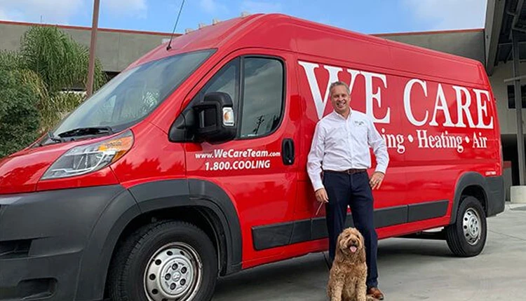 A man in a white shirt, smiling, stands next to a red van with We Care branding. A brown dog sits beside him. The scene is bright and friendly