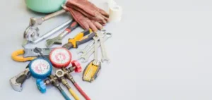 A variety of plumbing tools and equipment, including wrenches, gauges, pliers, gloves, and a pipe cutter—often used in Air Conditioning Repair—arranged on a light surface in Salt Lake City.