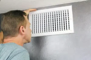A man in Salt Lake City, UT, inspects a white air vent mounted on a gray wall after an air duct installation.