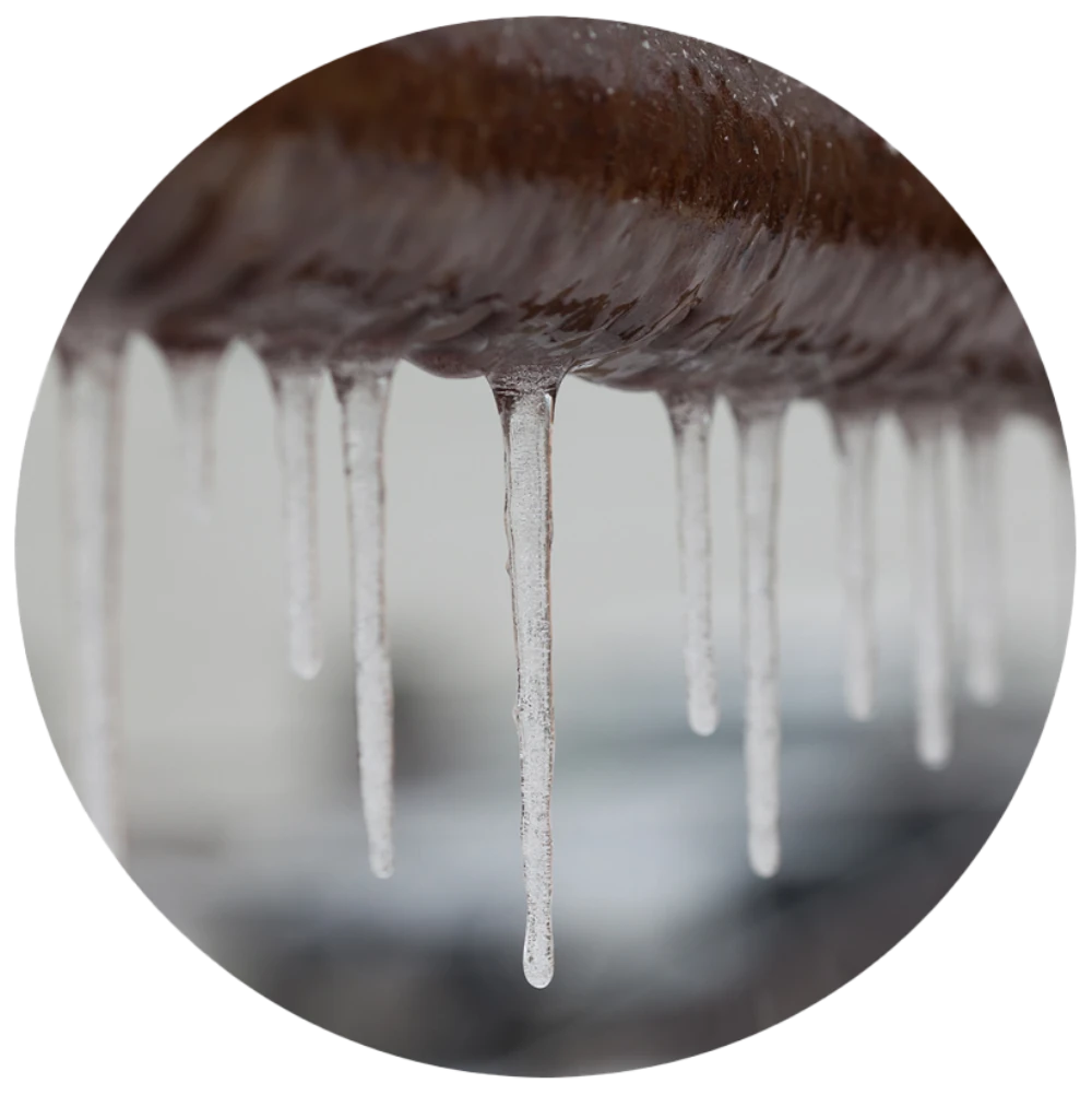 Icicles hanging from the edge of a brown metal pipe in winter, hinting at frozen pipes, with a blurred background.