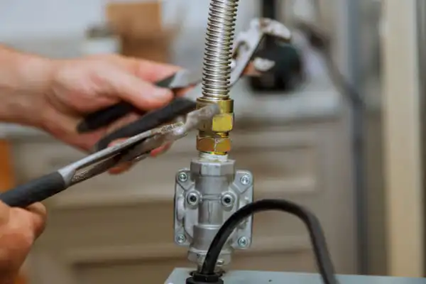 Hands using pliers to tighten a metal fitting on a flexible gas line connected to a valve during gas line installation in Salt Lake City.