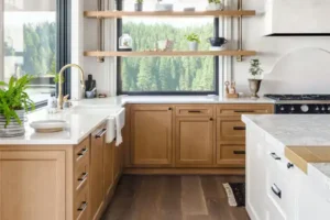 Modern kitchen with light wood cabinets, white countertops, a farmhouse sink perfect for Salt Lake City living, open shelves with plants, and a large window showing a forest view.