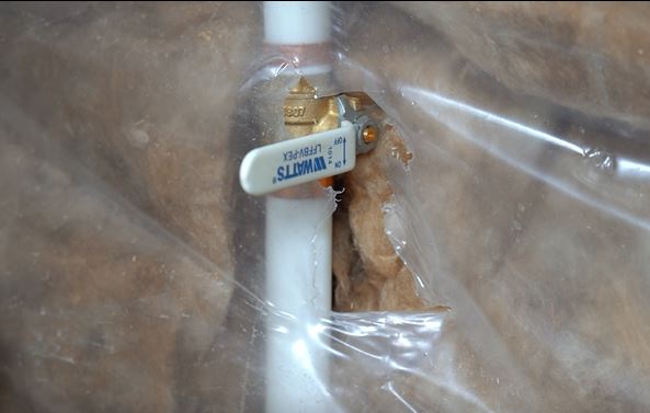 A close-up of a white PVC pipe with a brass shut-off valve labeled "WATTS," surrounded by insulation and clear plastic sheeting—an important feature for gas leak safety in any utility installation.