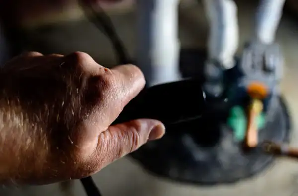 A close-up of a hand holding a black flashlight, aimed towards an out-of-focus area with pipes and a valve—ideal for inspecting spaces during Sump Pump Installation in Salt Lake City.