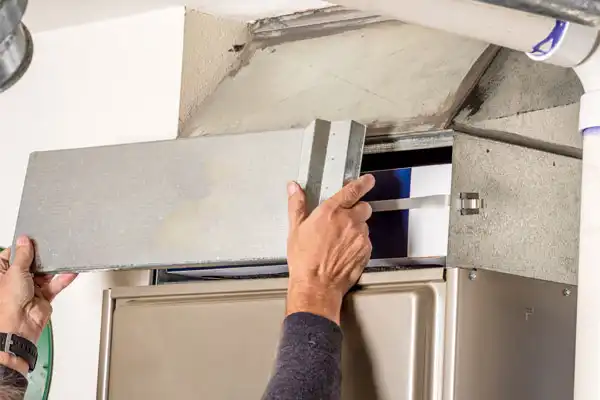 A person’s hands are removing the cover from a furnace to access and replace the air filter, demonstrating routine furnace maintenance in Salt Lake City.