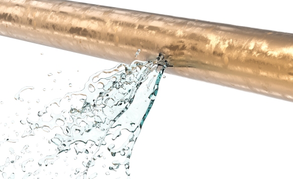 Water spraying out from a leak in a copper plumbing pipe against a white background.