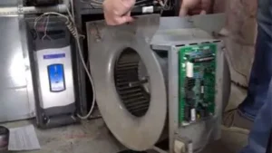 Person repairing or inspecting the blower motor assembly inside an HVAC furnace system, with exposed circuit board and wiring visible—checking for common furnace culprits behind frequent furnace problems and unexpected Furnace fails.