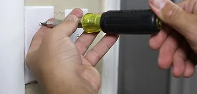 %Focuskw% | Any Hour Services A person uses a screwdriver to unscrew the cover of a wall electrical outlet while preparing for a light switch installation.
