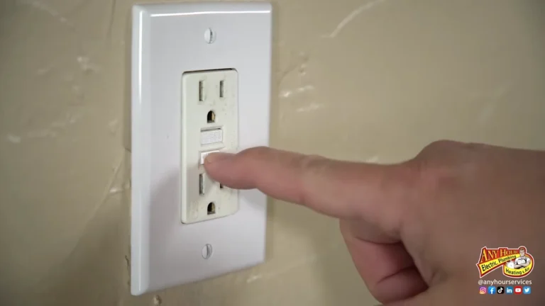 A person presses the test button on a GFCI electrical outlet mounted on a beige wall.