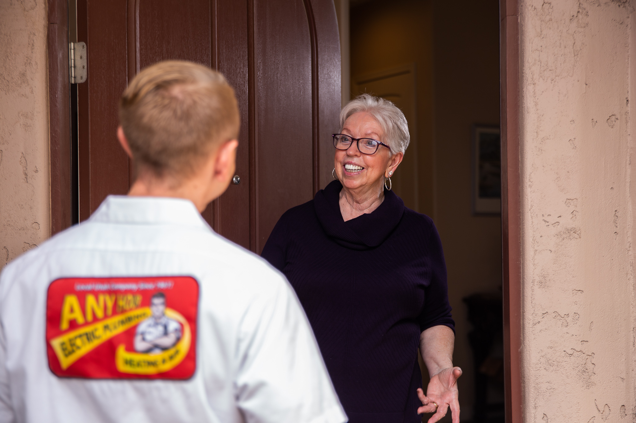 %Focuskw% | Any Hour Services- Electric, Plumbing, Drains, Heating &Amp; Air An electrician in uniform stands at the door, speaking with an older woman who is smiling and standing inside her home, discussing how recessed lighting can enhance her home's ambiance.