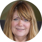 %Focuskw% | Any Hour Services A woman with long, light brown hair and bangs is smiling slightly while looking at the camera. She is indoors, with a blurred background.