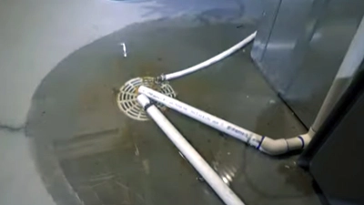 %Title% | Any Hour Services Two white PVC pipes lead into a floor drain, with water pooling on the gray floor—possible sewer problems or early sewer line signs.