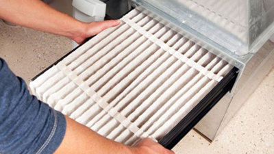 A person inserts a clean furnace filter into a compartment of an HVAC system—an essential step in furnace maintenance.