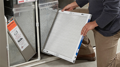 A person is installing or removing a rectangular furnace filter from a residential HVAC system during routine furnace maintenance.
